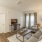 Spacious and well lit living room with wood flooring, large windows and open access to the kitchen